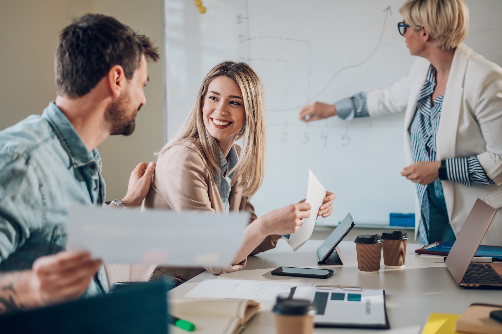 Business team on a meeting in a modern bright industrial design office interior. Team leader present project to its diverse colleagues. Focus on a blonde beautiful woman smiling.