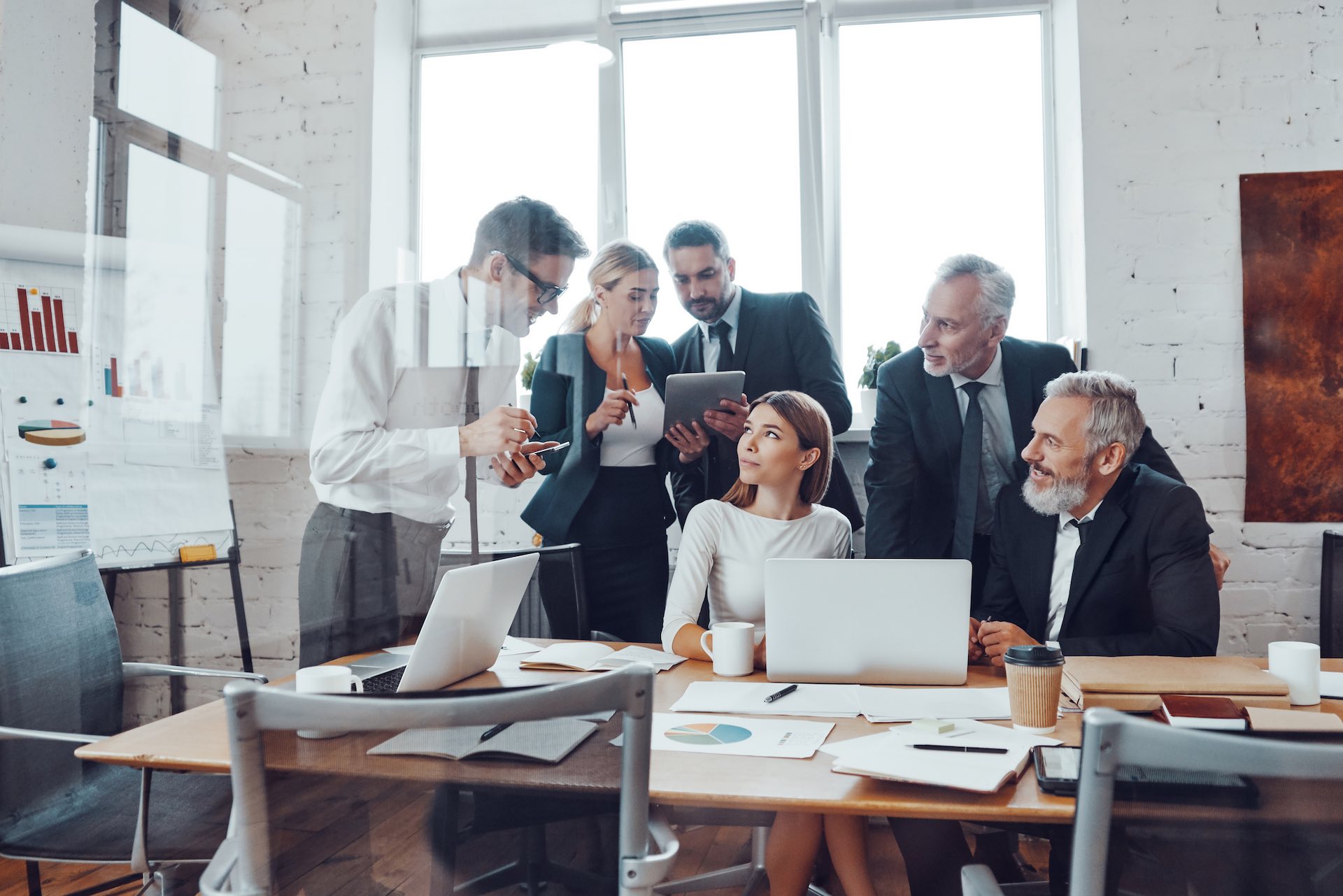 Professional business team analyzing sales using modern technologies while having staff meeting in the board room Professional business team analyzing sales using modern technologies while having staff meeting in the board room