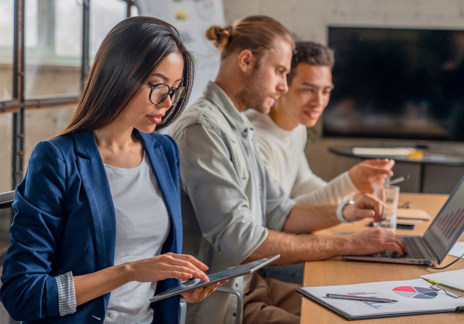 Asian female working on digital tablet. Young businessman in meeting with coworkers in conference room. Creative professionals discussing business in board room