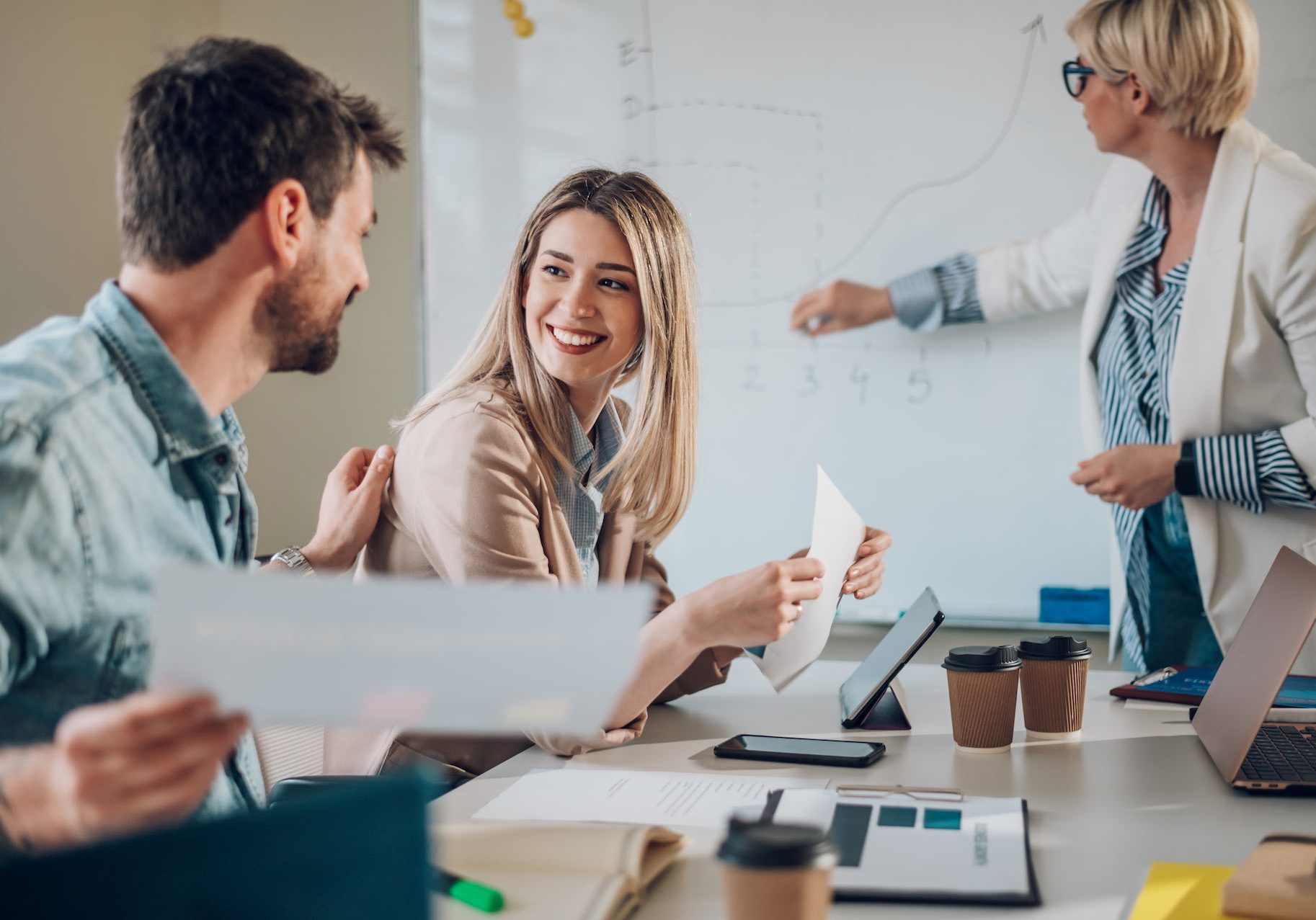 Business team on a meeting in a modern bright industrial design office interior. Team leader present project to its diverse colleagues. Focus on a blonde beautiful woman smiling.